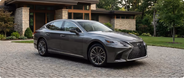 Gray Lexus sedan parked on a stone driveway in front of a modern house with stone and wood exterior.