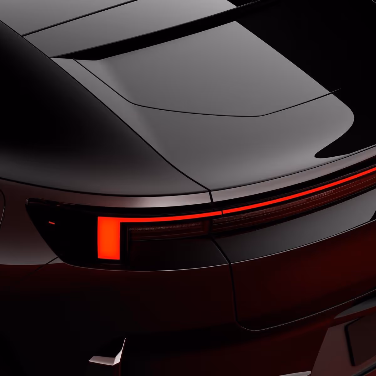 Close-up of a sleek black car's rear with modern red LED tail lights illuminated.