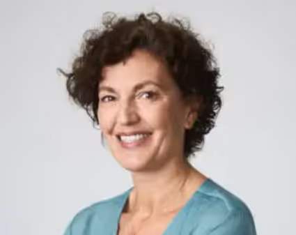 Smiling woman with short curly dark hair wearing a teal top against a light background.