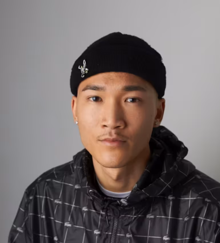 Portrait of a young man wearing a black beanie and checkered jacket against a gray background.