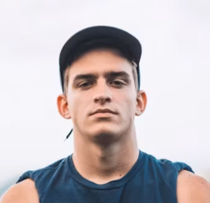 Young man in a sleeveless navy shirt and black cap looking directly at the camera.