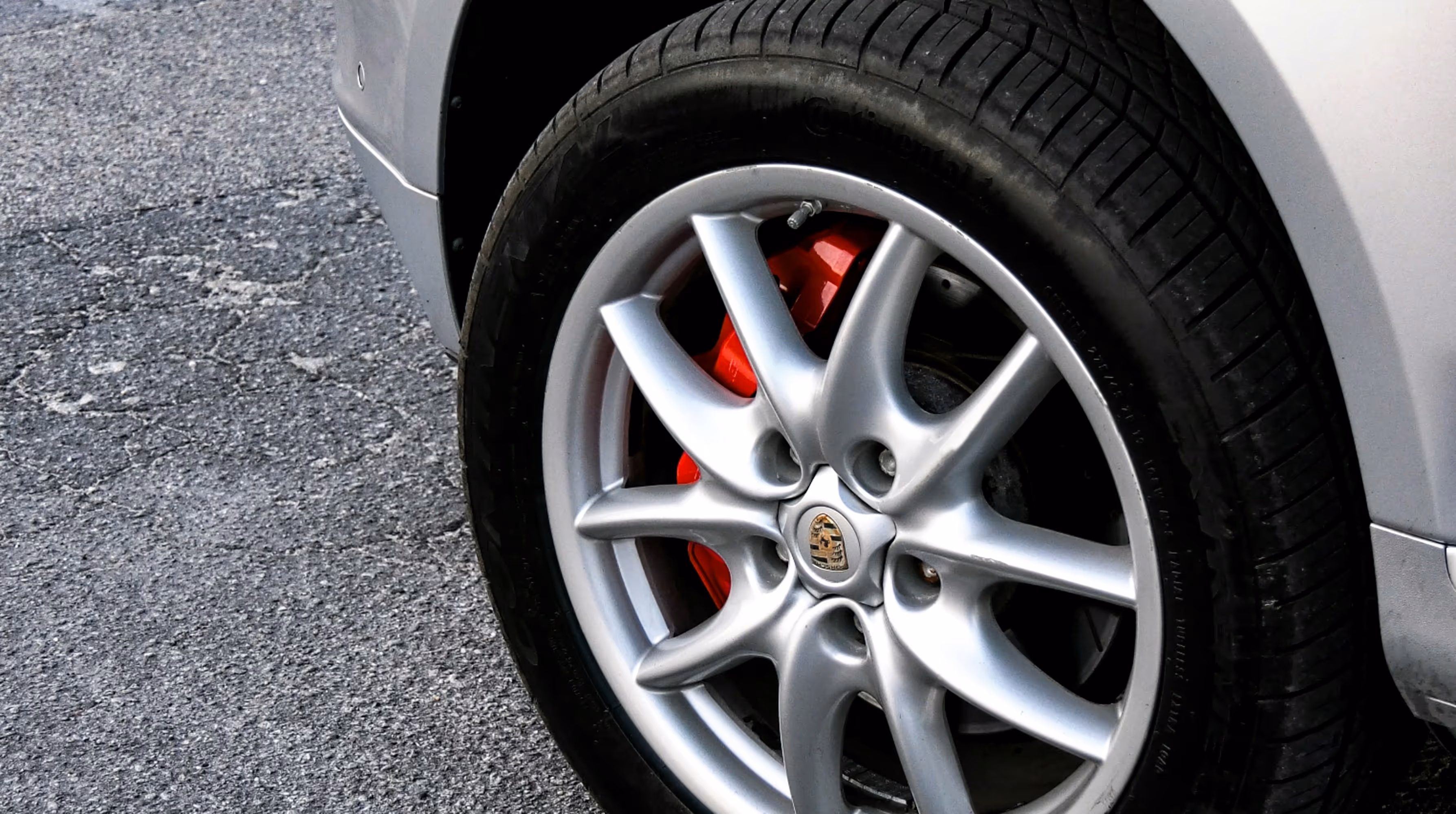 Close-up of a Porsche car wheel with silver alloy rim and red brake caliper on asphalt.
