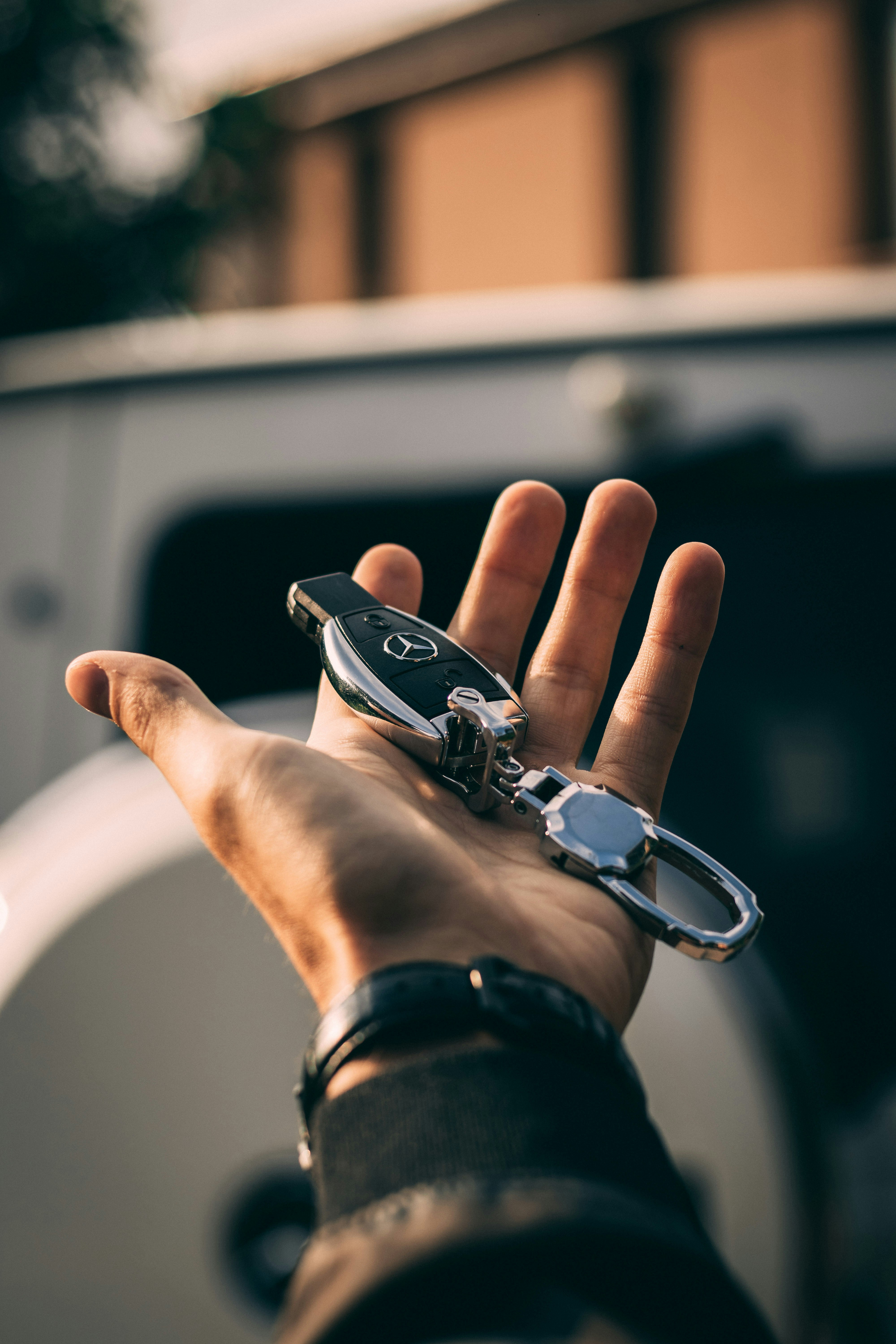 Hand holding a Mercedes car key fob with a blurred vehicle background.