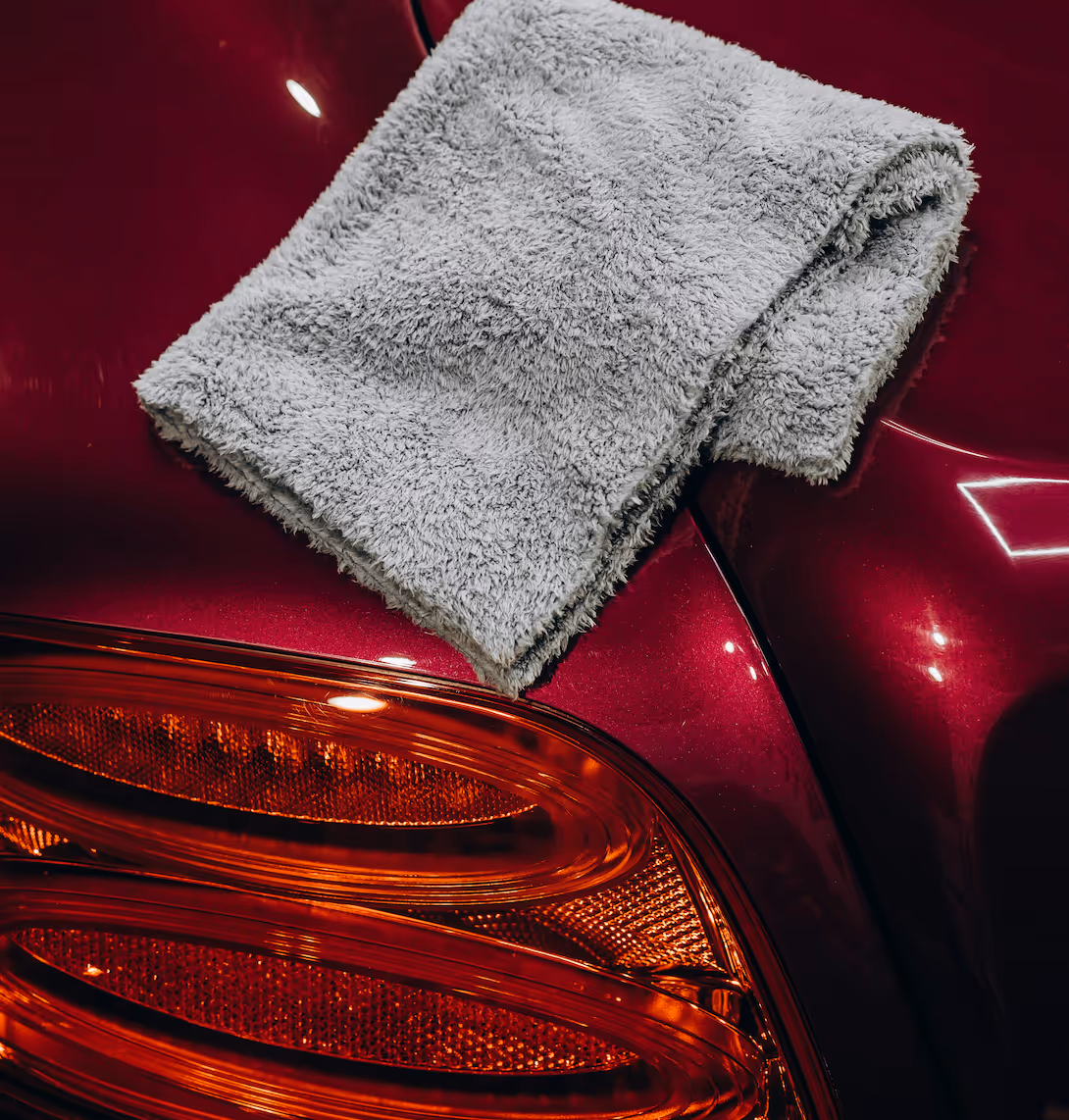 Gray microfiber cloth on the red shiny surface of a car near its rear light.
