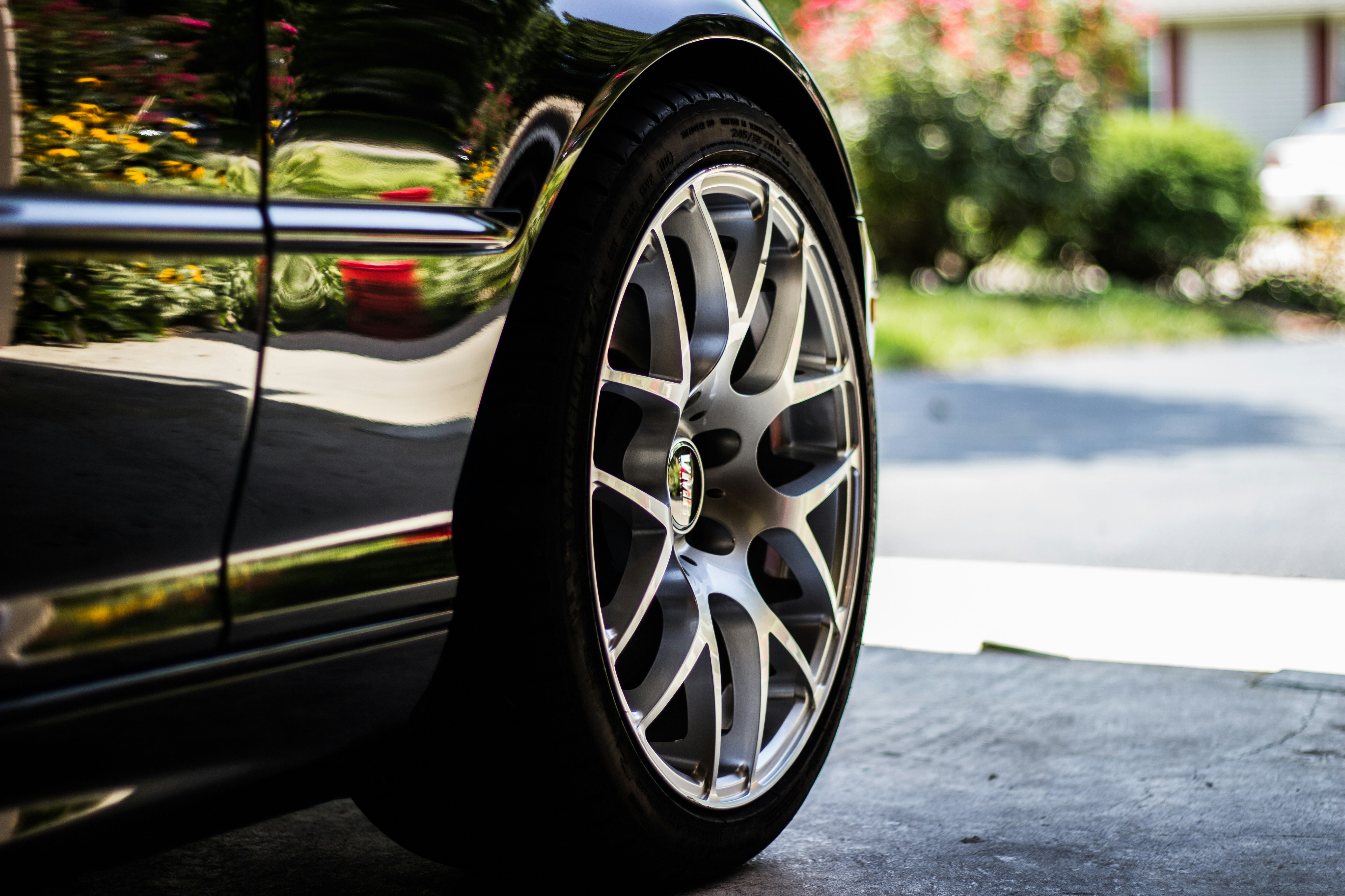 Close-up of a black car's shiny side and silver alloy wheel with a low-profile tire.