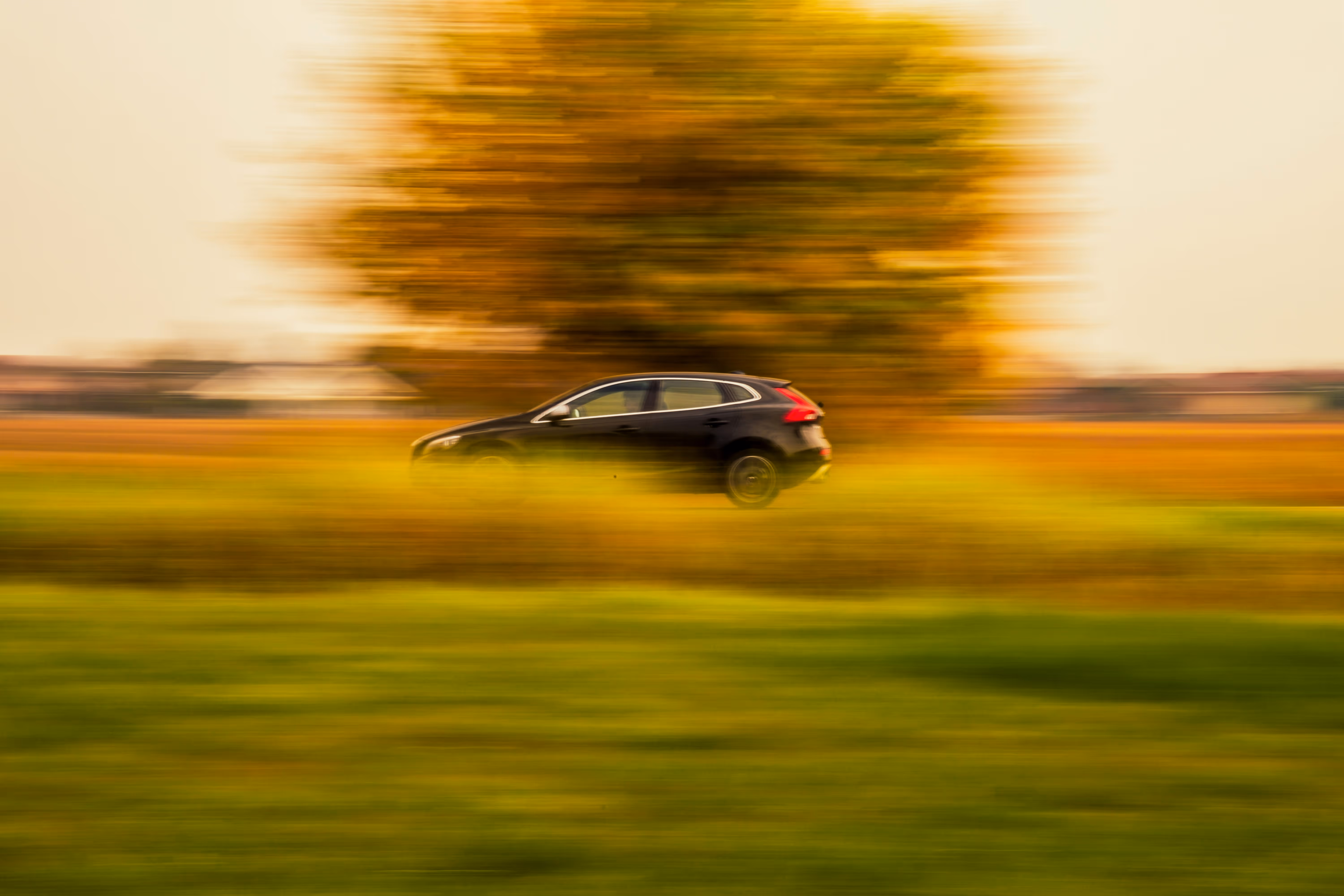 Black car driving fast with a blurred autumn landscape of green and yellow fields and tree.