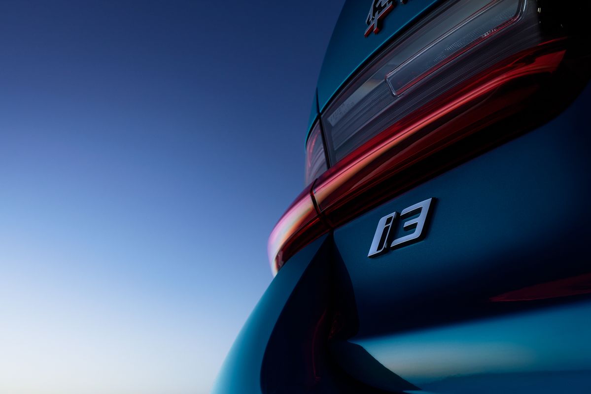 Close-up of the rear end of a blue car with an 'i3' badge and red taillight against a clear blue sky.