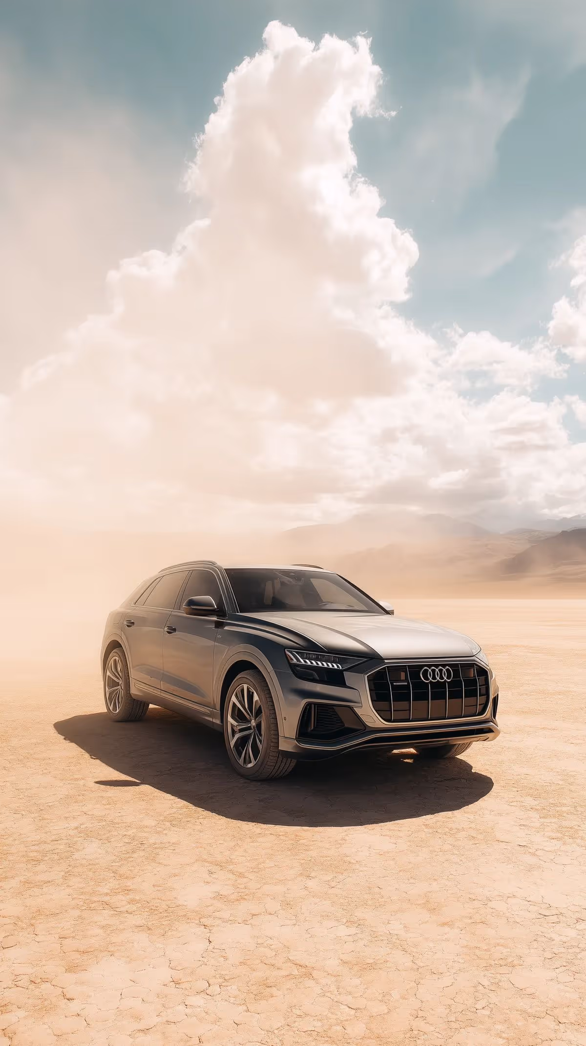 Silver Audi SUV parked on a dry, cracked desert landscape with large clouds in a blue sky.