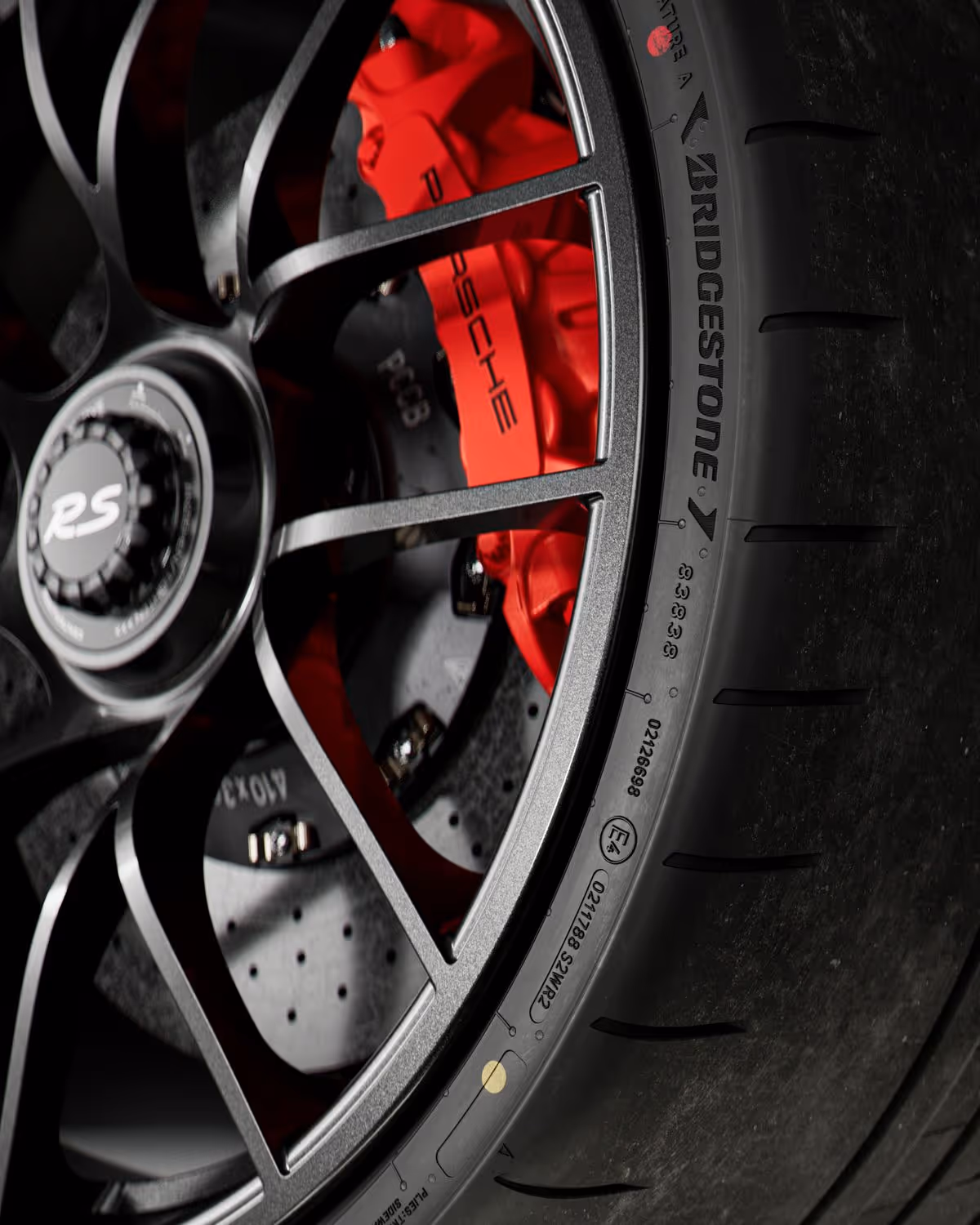 Close-up of a Porsche car wheel with black alloy rim, red brake caliper, drilled brake disc, and Bridgestone tire.