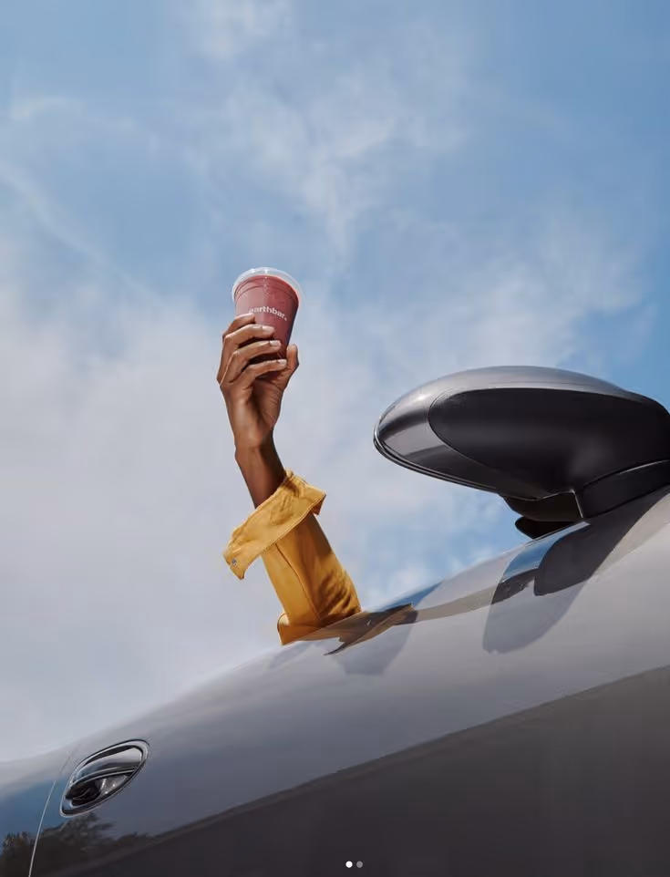 Person wearing a yellow sleeve holding a red cup out of a car window against a blue sky.