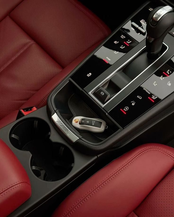 Car center console with red leather seats, gear shifter, cup holders, and a Porsche Macan key fob.