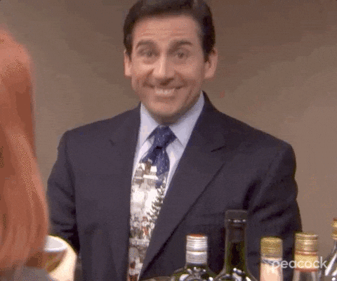 Man in a suit sitting at a table with various bottles, smiling nervously.