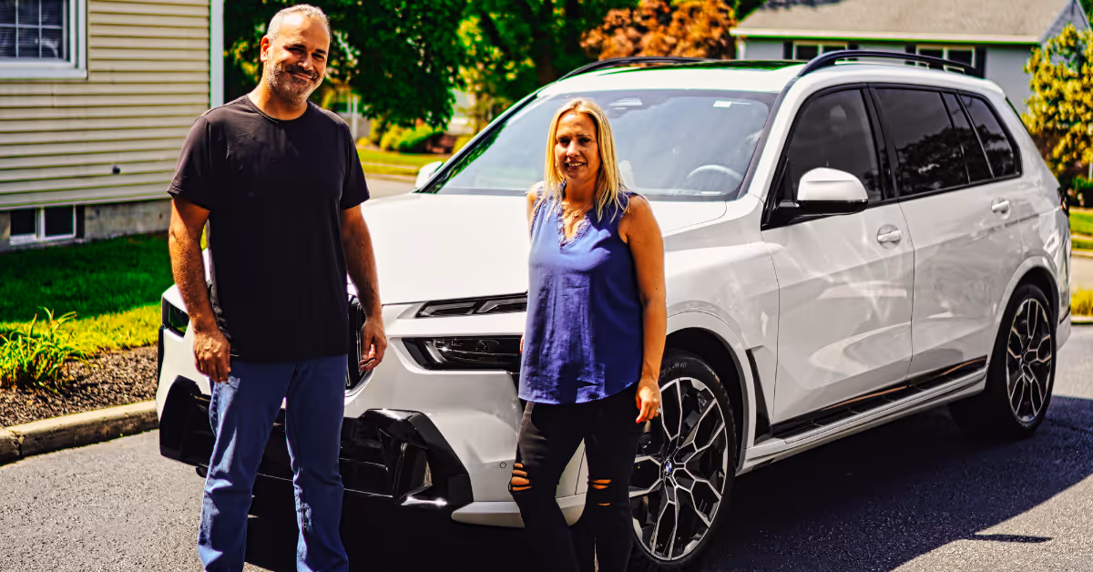 Man and woman standing next to a white SUV parked in a residential driveway.