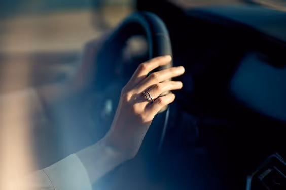 Close-up of a hand wearing a ring resting on a car steering wheel.