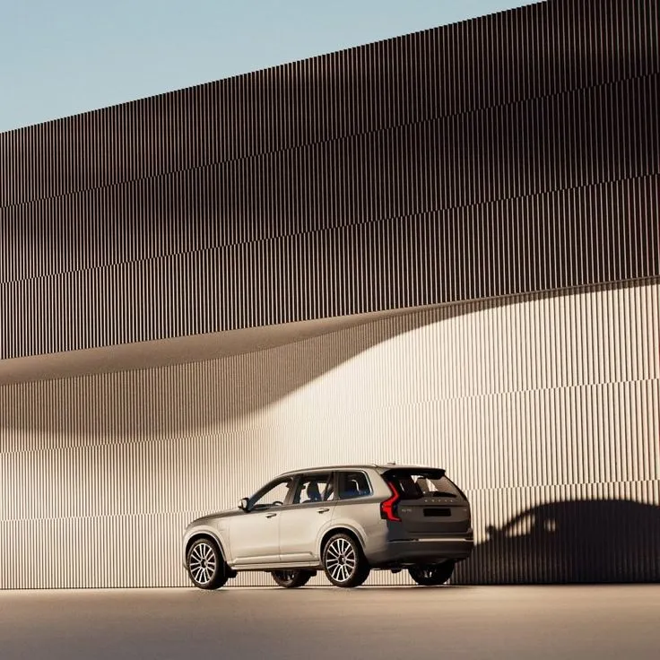 Silver SUV parked in front of a modern building with vertical ridged facade casting shadows.