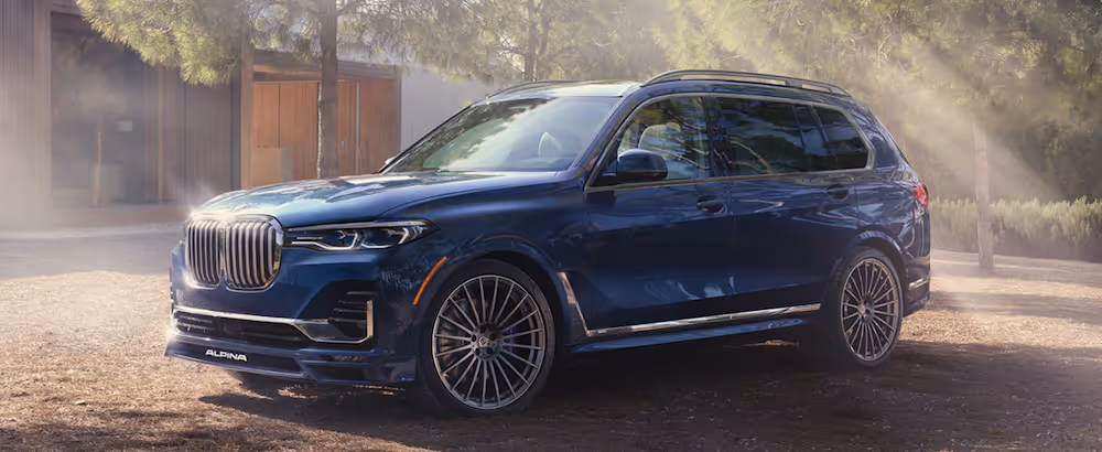 Dark blue BMW SUV parked on a dirt driveway with sunlight filtering through surrounding trees.