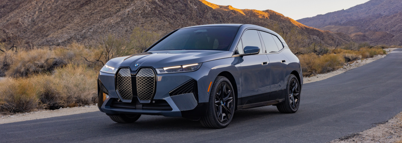 Gray BMW electric SUV parked on a desert road with mountains in the background during sunset.