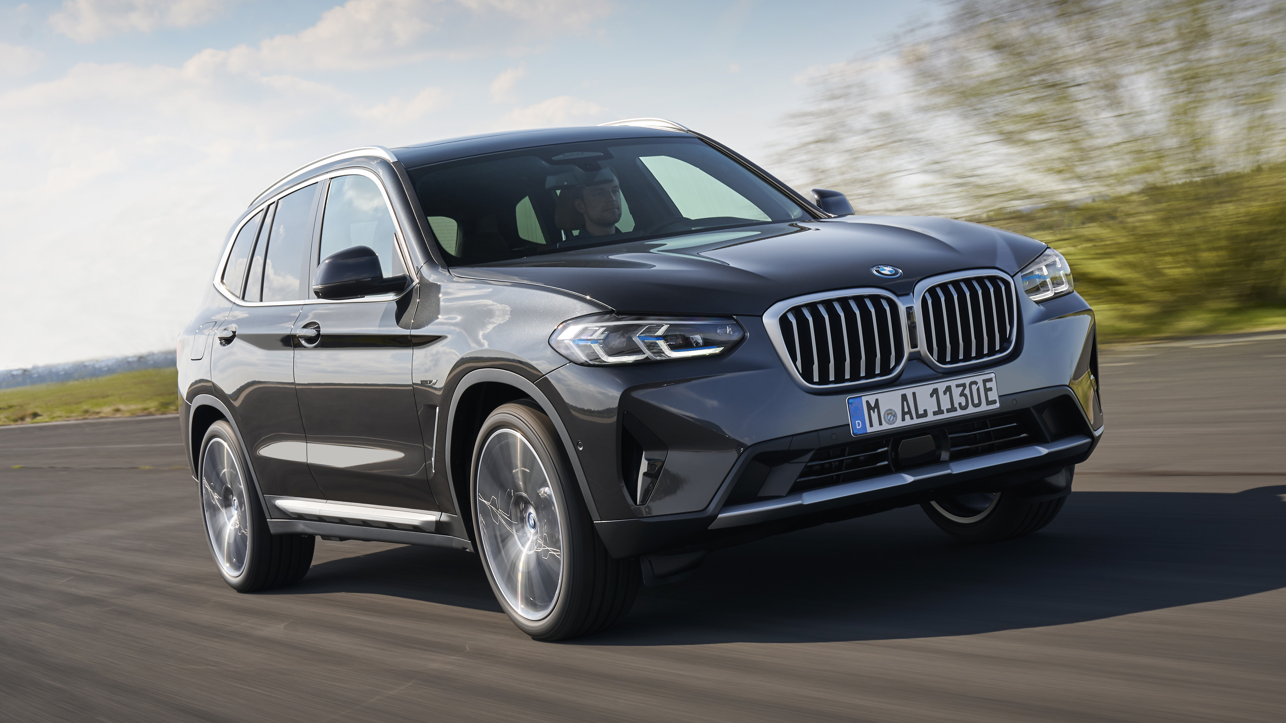 Black BMW X3 SUV driving on a road with blurred background and driver visible inside.