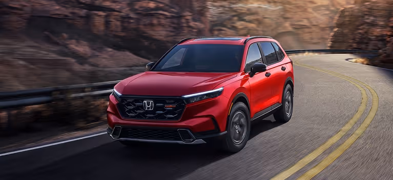 Red 2026 Honda CR-V TrailSport Hybrid driving on a winding mountain road.
