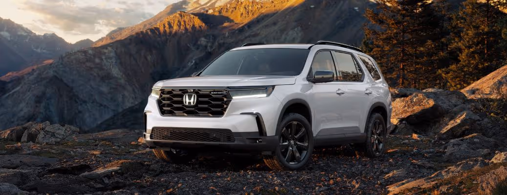 Silver Honda SUV parked on rocky terrain with mountains and trees in the background at sunset.